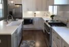 This kitchen showcases a modern and clean design with a blend of white cabinetry, stainless steel appliances, and a sleek layout